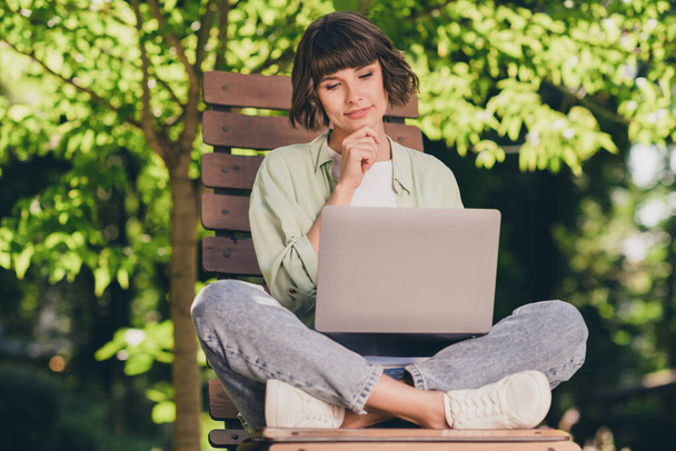 Full length body size photo smiling young girl sitting on bench working on computer thoughtful - 写真・画像