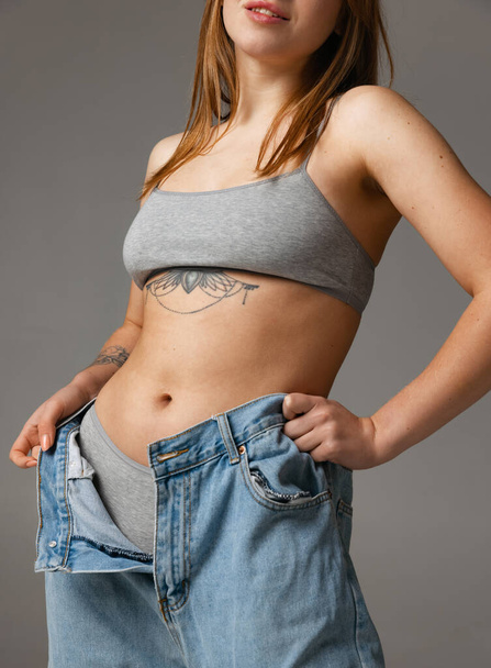 Cropped portrait of young beautiful slim woman in blue jeans jumpersuit posing isolated over gray studio background. Weight Loss concept. - Foto, afbeelding