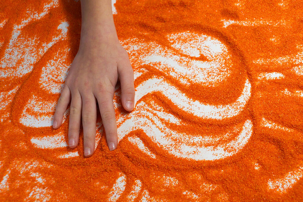 sesión de terapia de arena, la mano de un niño toca la arena naranja. - Foto, imagen