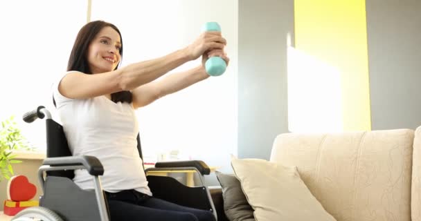 Mujer sonriente haciendo ejercicios de mano con pesas mientras está sentado en silla de ruedas de cámara lenta 4k película - Metraje, vídeo