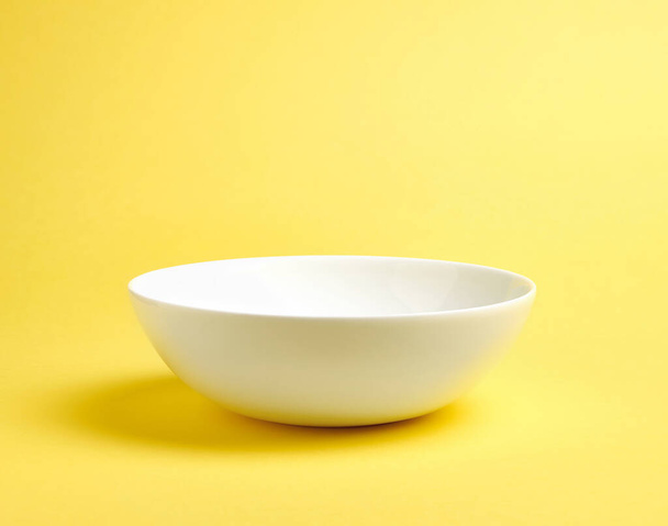 Empty white ceramic bowl on yellow background - Foto, imagen