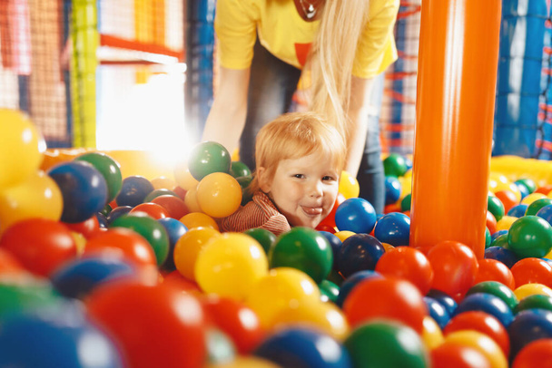 Niño feliz jugando en Ball Pool. Niño divirtiéndose con joven madre en parque infantil piscina de bolas - Foto, Imagen