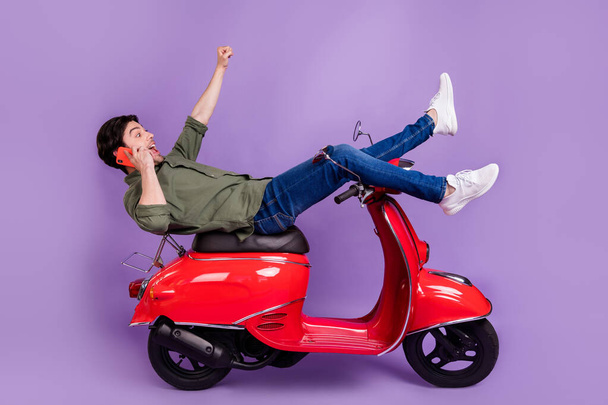 Full length photo of amazed brunette man winner rider wear jeans phone talk crazy isolated on purple color background - Photo, image