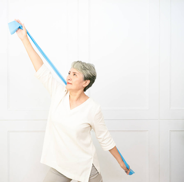 Senior asian woman doing exercises with resistance band at home. - Фото, изображение