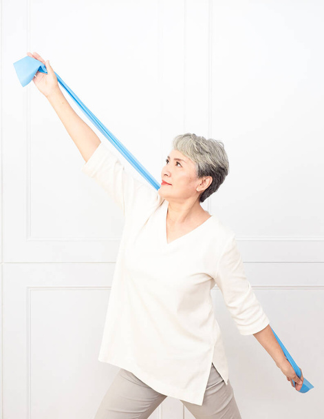 Senior asian woman doing exercises with resistance band at home. - Фото, изображение