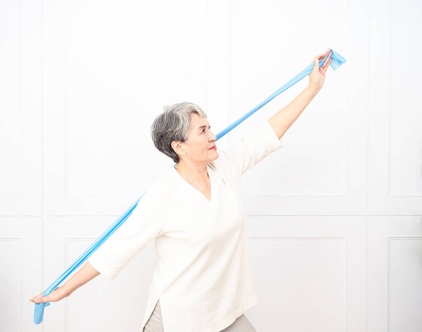 Senior asian woman doing exercises with resistance band at home. - Foto, Bild
