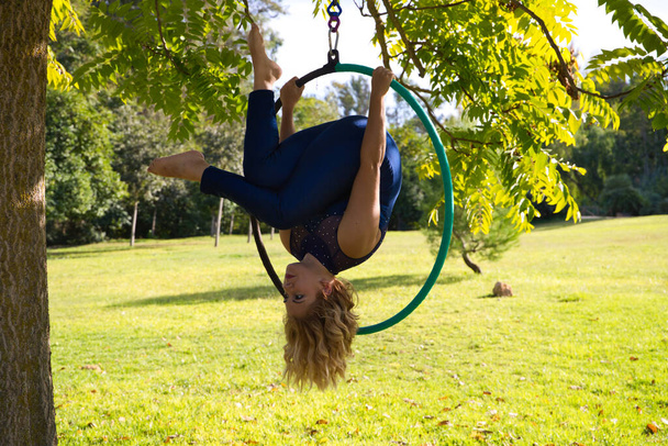 Blondynka i młoda gimnastyczka akrobatka uprawiają sport powietrzny na świeżym powietrzu w parku. Lite kobieta w niebieskim kostiumie wykonuje pozy cyrkowych wykonawców tańczących z biodrami. - Zdjęcie, obraz