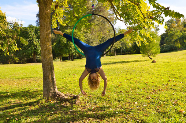 Blonde woman and young gymnast acrobat athlete performing aerial exercise on air ring outdoors in park. Lithe woman in blue costume performs poses of circus performers dancing with hips. - Photo, Image