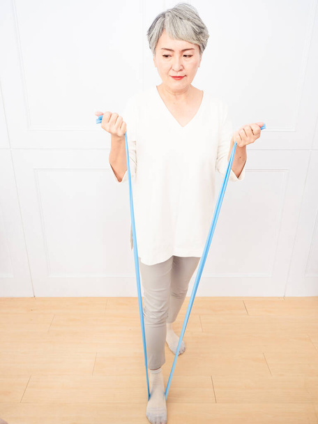 Senior asiatique femme faire des exercices avec résistance bande à la maison. - Photo, image