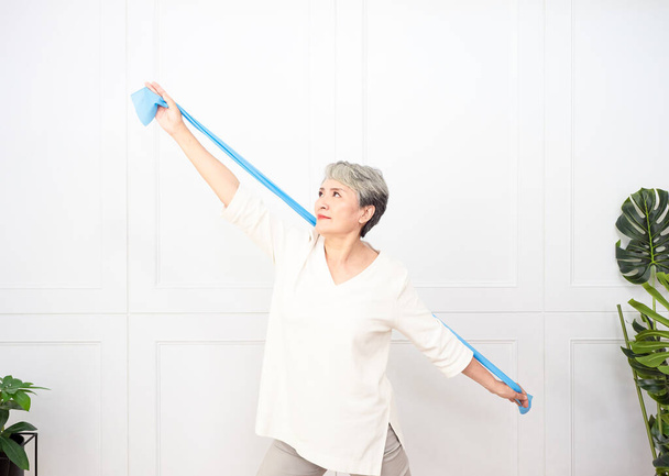Senior asiático mujer haciendo ejercicios con resistencia banda en casa. - Foto, imagen