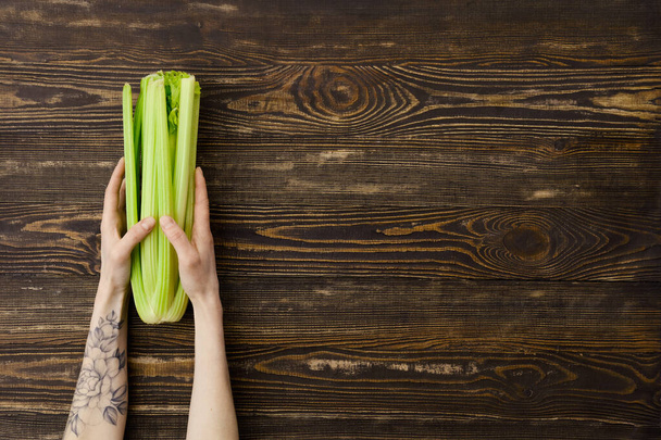 Overhead view of fresh celery in hand over wooden background - Fotografie, Obrázek
