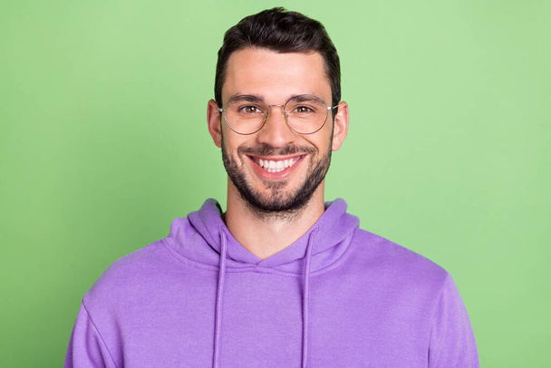 Photo of nice young brunet guy wear eyewear violet hoodie isolated on green color background - Foto, imagen