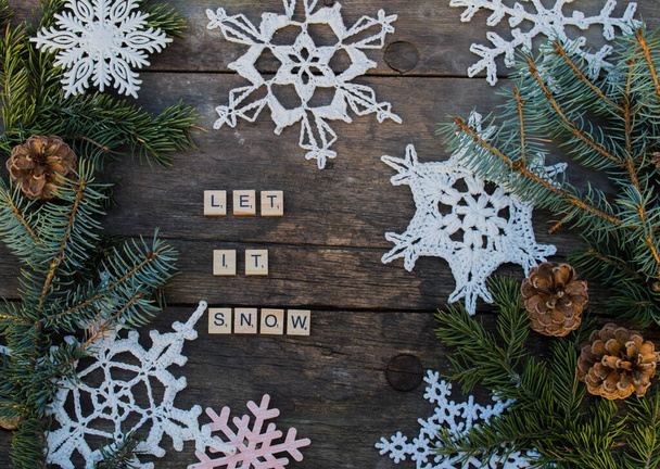 βελονάκι νιφάδες χιονιού σε ξύλινο έδαφος με χειμερινά συνθήματα και κλαδιά ελάτης και κώνους ξύλινα γράμματα φόντο - Φωτογραφία, εικόνα
