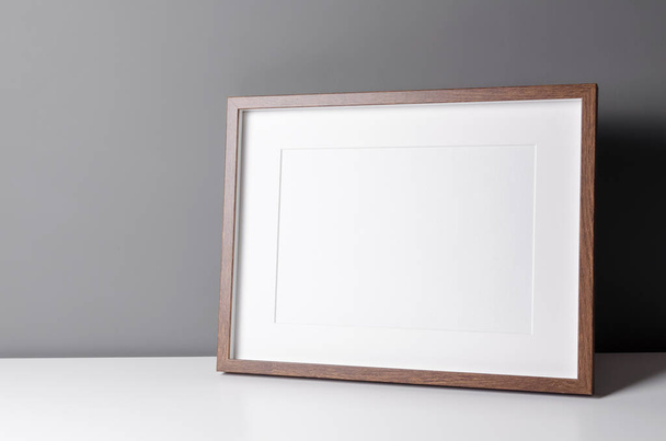 Landscape wooden frame mockup for artwork, photo and print presentation on white table over grey wall. Minimalist interior design. - Foto, afbeelding