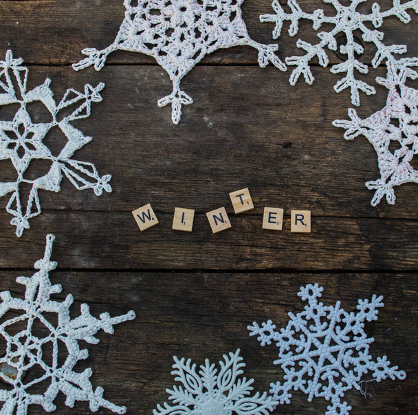 crochet snowflake ornaments on wooden ground with winter slogans and fir branch and cones  wooden letters background - Foto, imagen