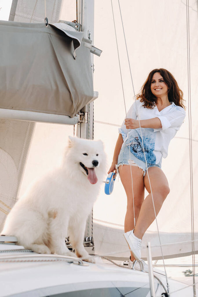 eine glückliche Frau mit einem großen weißen Hund auf einer weißen Jacht im Meer. - Foto, Bild