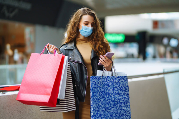 Stylish woman in protective mask after shopping. Black friday. Consumerism, purchases, sale, lifestyle, tourism concept. - Фото, изображение