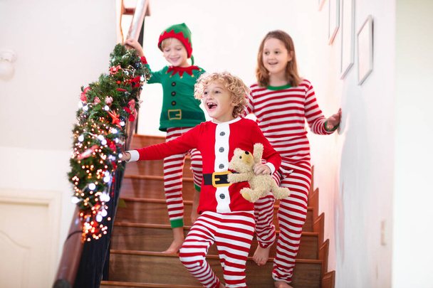 Dzieci biegające po schodach w świąteczny poranek. Dzieci w piżamie uciekają na dół z chęcią otworzenia prezentów świątecznych. Świętowanie w domu. Zimowe rodzinne wakacje. Chłopiec i dziewczyna otwierając prezenty. - Zdjęcie, obraz
