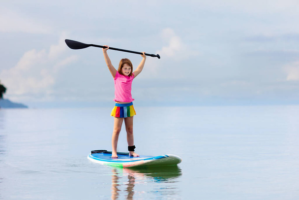 Child on stand up paddle board. Water fun and beach sport for kids. Healthy outdoor sports for summer vacation on tropical island. Holiday activity. Fit little girl training. Surfer exercising. - Fotoğraf, Görsel