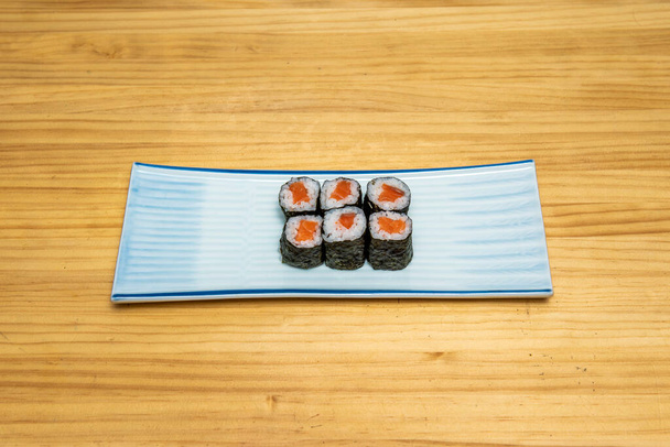 Norwegisches Lachs-Hosomaki-Sushi mit Reis gewürzt mit japanischem Essig in Nori-Algen auf blauem Teller - Foto, Bild