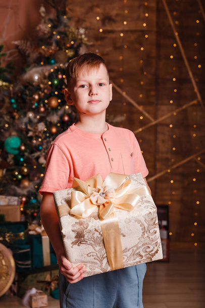 teenage boy holding a large box with gift against the background of a Christmas tree - Valokuva, kuva