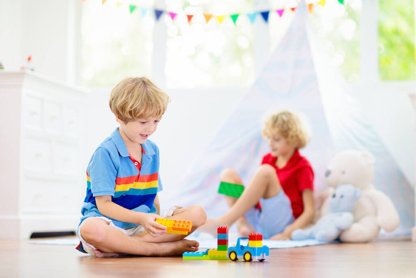 Kids room with teepee tent. Children play in white sunny bedroom. Cozy light interior for kid nursery or playroom. Little boy with toy blocks and dinosaur playing on wooden floor. Home decoration. - Photo, Image