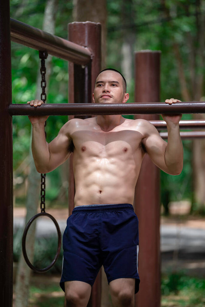 Handsome man exercises by hanging on a bar outdoor,  Asian man trains for sporting events - Fotó, kép
