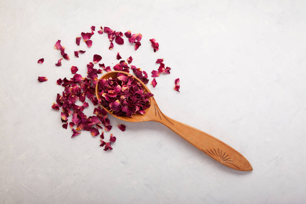 Dried rose petals in a wooden spoon, top view. Light background, copy space. Pink colored organic herb used for perfumes, cosmetics, teas and baths. - Foto, immagini