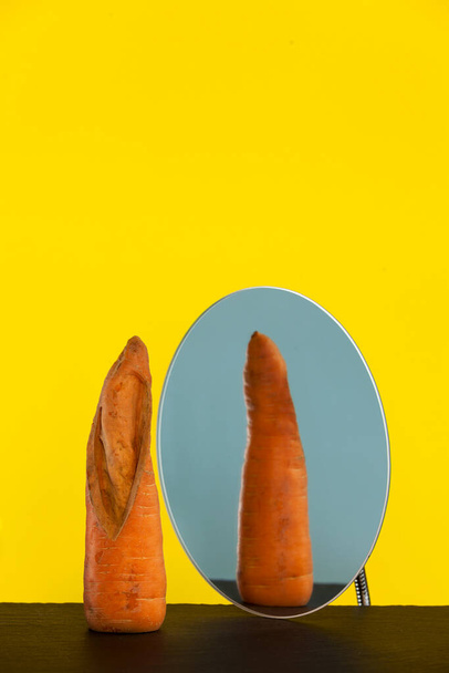 Ugly carrot in front of mirror, reflection, reverse side. Concept - reduction of organic food waste. Crooked vegetables and fruits can be eaten. - Foto, Imagem