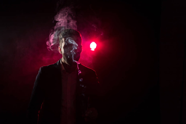 Photo of man with cigarette lighter on black background and pink light. - Foto, Bild
