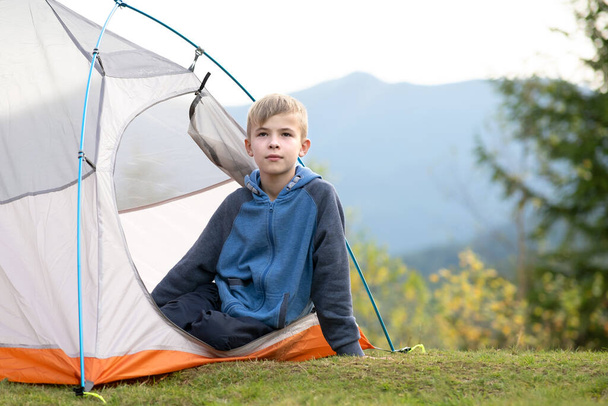 Wanderer-Kind ruht sich in einem Zeltlager auf einem Bergcampingplatz aus und genießt die Aussicht auf die sommerliche Natur. - Foto, Bild