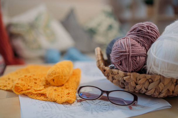 Casa hobbies: Tricô e crochê. Bolas de lã em uma cesta, acessórios de tricô, padrões de crochet, começou a tricotar e óculos na mesa. - Foto, Imagem