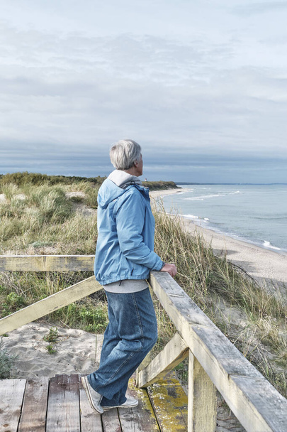 Starší žena s krátkými šedými vlasy dřevěnou plošinu u moře.. Cestovní koncept - Fotografie, Obrázek