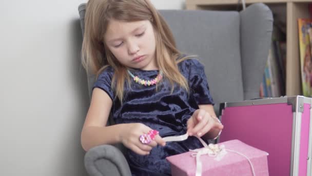 Triest elegant klein meisje in een fluwelen jurk en ringen om haar vingers zit thuis in een stoel - Video
