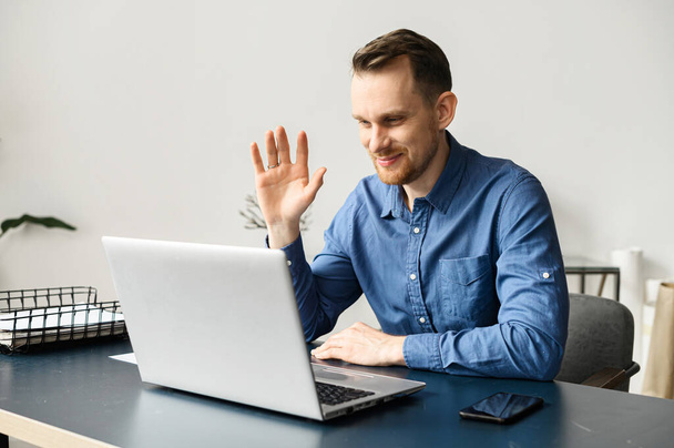 Cheerful male office employee in smart casual wear waving into webcam - 写真・画像