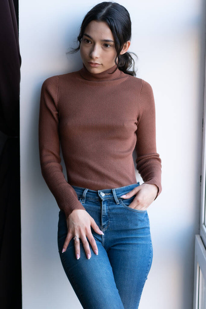 Stüdyodaki genç ve güzel bir kadının portresi, kot pantolonun içinde duruyor. - Fotoğraf, Görsel