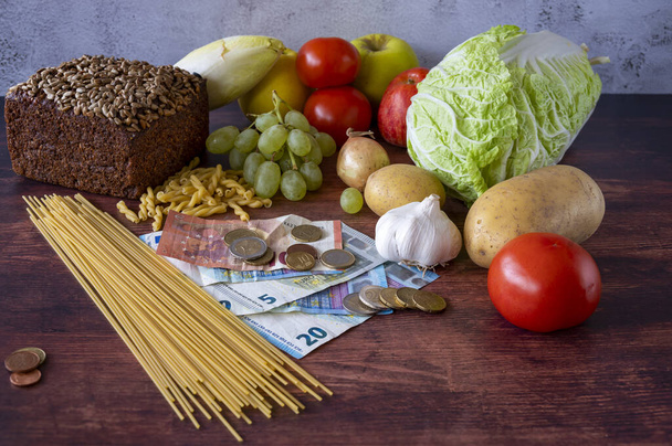 Food lies on a wooden table along with European banknotes and coins symbolizing inflation. - Photo, Image