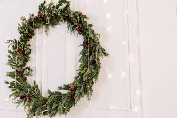 Décorations pour la nouvelle année, une couronne de branches de sapin sur le mur. Couronne décorative de Noël dans une maison confortable - Photo, image