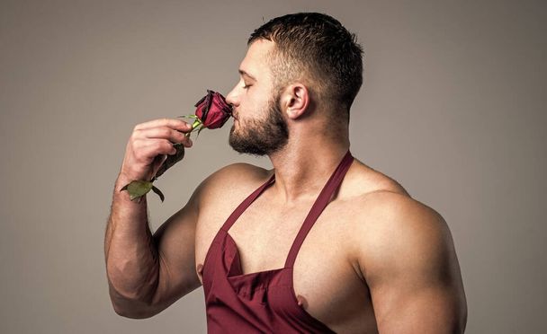handsome man wear cook apron smelling red rode fower, romance - Фото, изображение