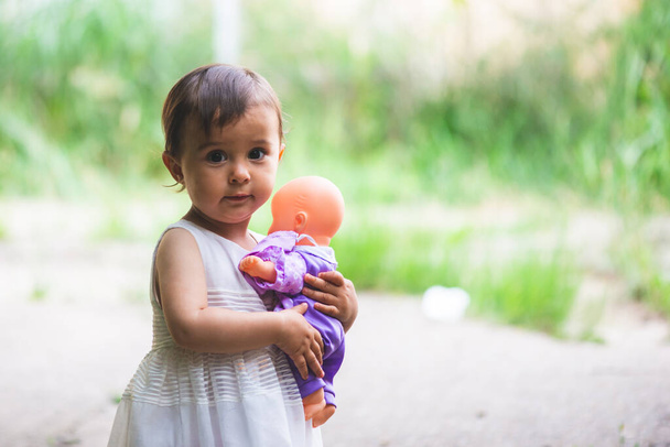 Cutte petite fille avec robe blanche tenir sa petite poupée dans ses bras - Photo, image