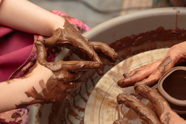 Dziecko pleśni z gliny garnek na kole garncarskim. Dorośli pomagają dziecku pracować z gliną. - Zdjęcie, obraz