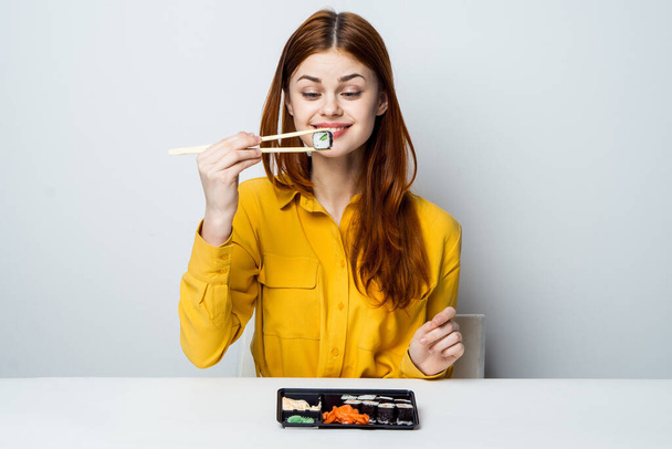 a woman in a yellow shirt sits at a table and eats sushi - Foto, afbeelding