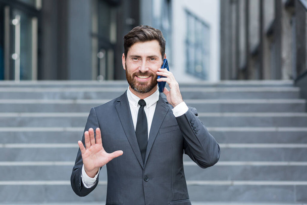 portrait successful young confident businessman talking background urban modern office building in downtown Bearded business man conversation a mobile phone standing in formal suit outdoor city street - Valokuva, kuva