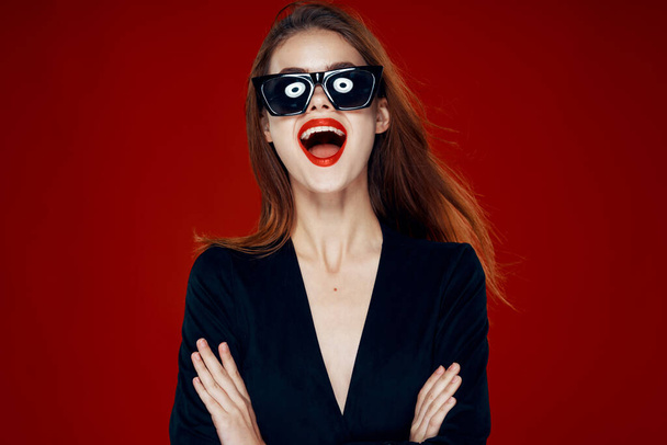cheerful fashionable woman wearing sunglasses red lips posing red background - Photo, Image