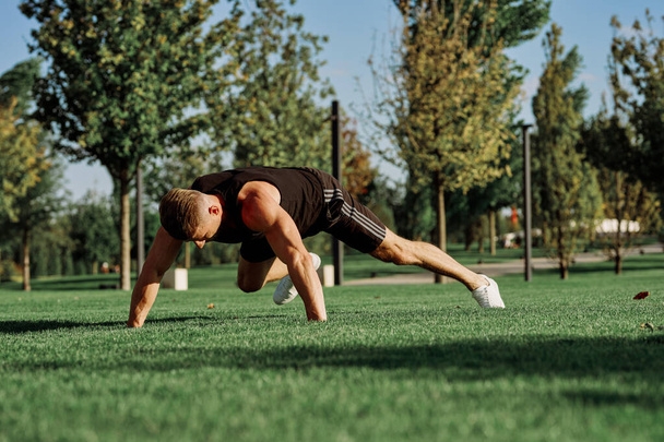 sports man doing exercises on the lawn in the park - Foto, Imagen