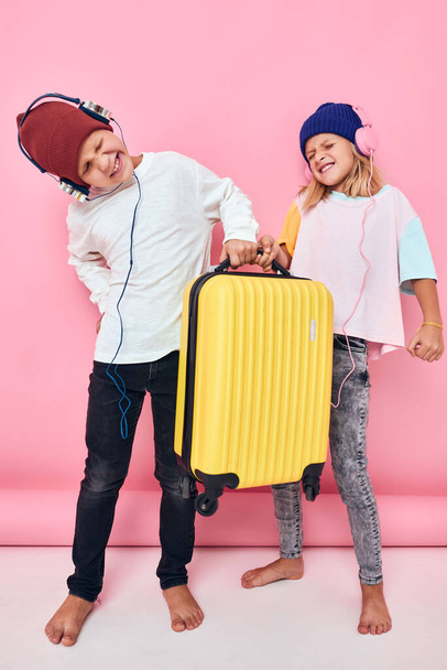 funny little boy and girl with a yellow suitcase in his hands studio posing - Фото, изображение
