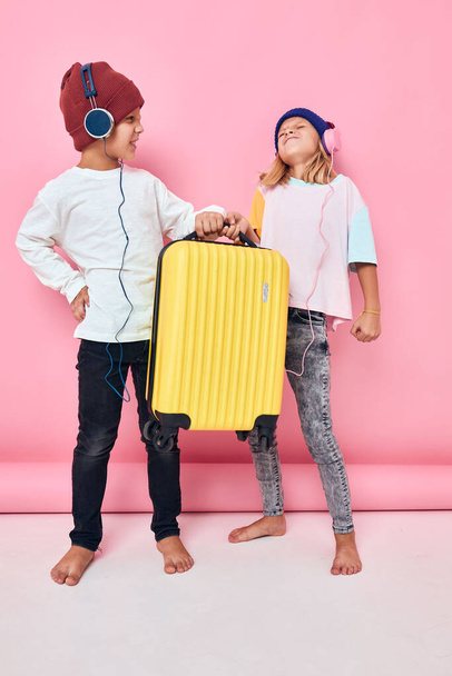 радісний хлопчик і дівчинка жовта валіза з навушниками концепція дитячого способу життя
 - Фото, зображення