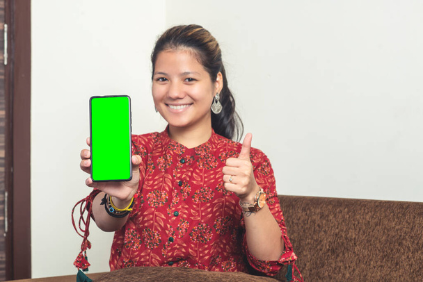 Young indian girl showing her mobile phone with green screen. Indian girl in traditional clothes with a mobile phone. - Photo, image