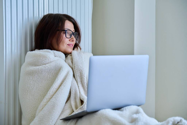 Woman working at home with laptop, warming with blanket and heating radiator - Foto, Imagem