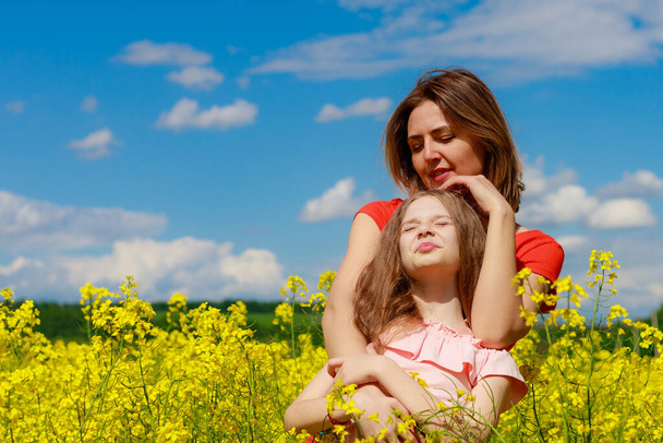 Mom and daughter in nature outdoors lifestyle. Cheerful lightning yellow color of blooming rapeseed field on the background. Positive emotion concept. - Photo, Image